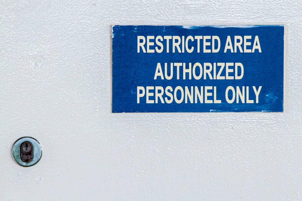 A blue sign on a white wall reads RESTRICTED AREA AUTHORIZED PERSONNEL ONLY; a lock is visible to the left of the sign.